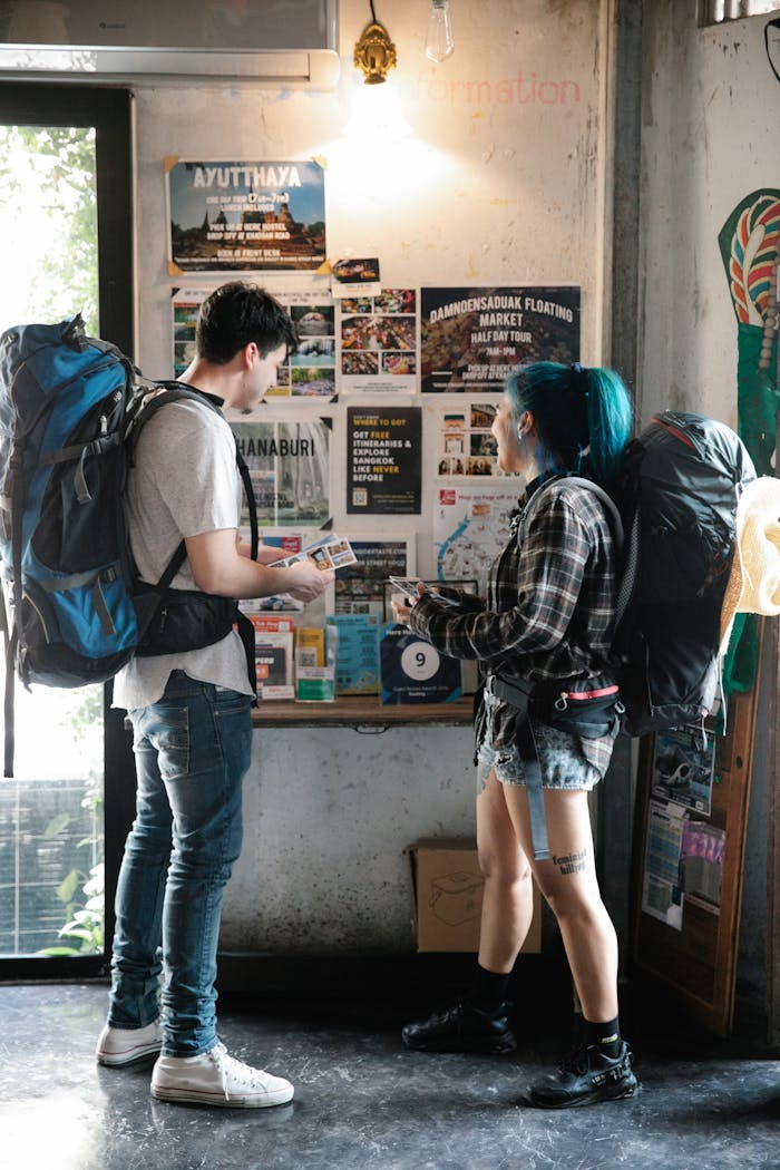 Home A young couple with backpacks examining travel brochures indoors, planning their next urban adventure.